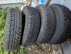 Four stacked used car tires on ground