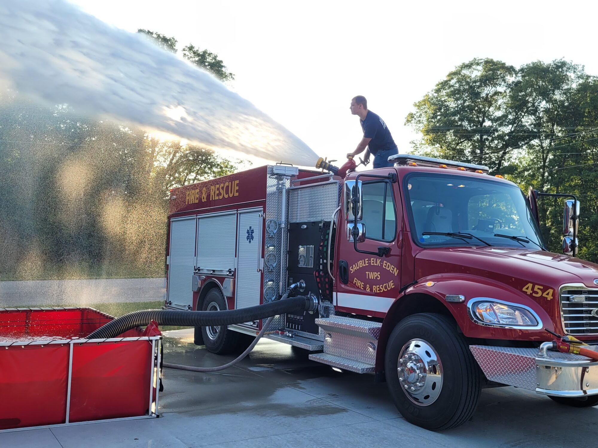 Firefighter training with fire truck and water hose.