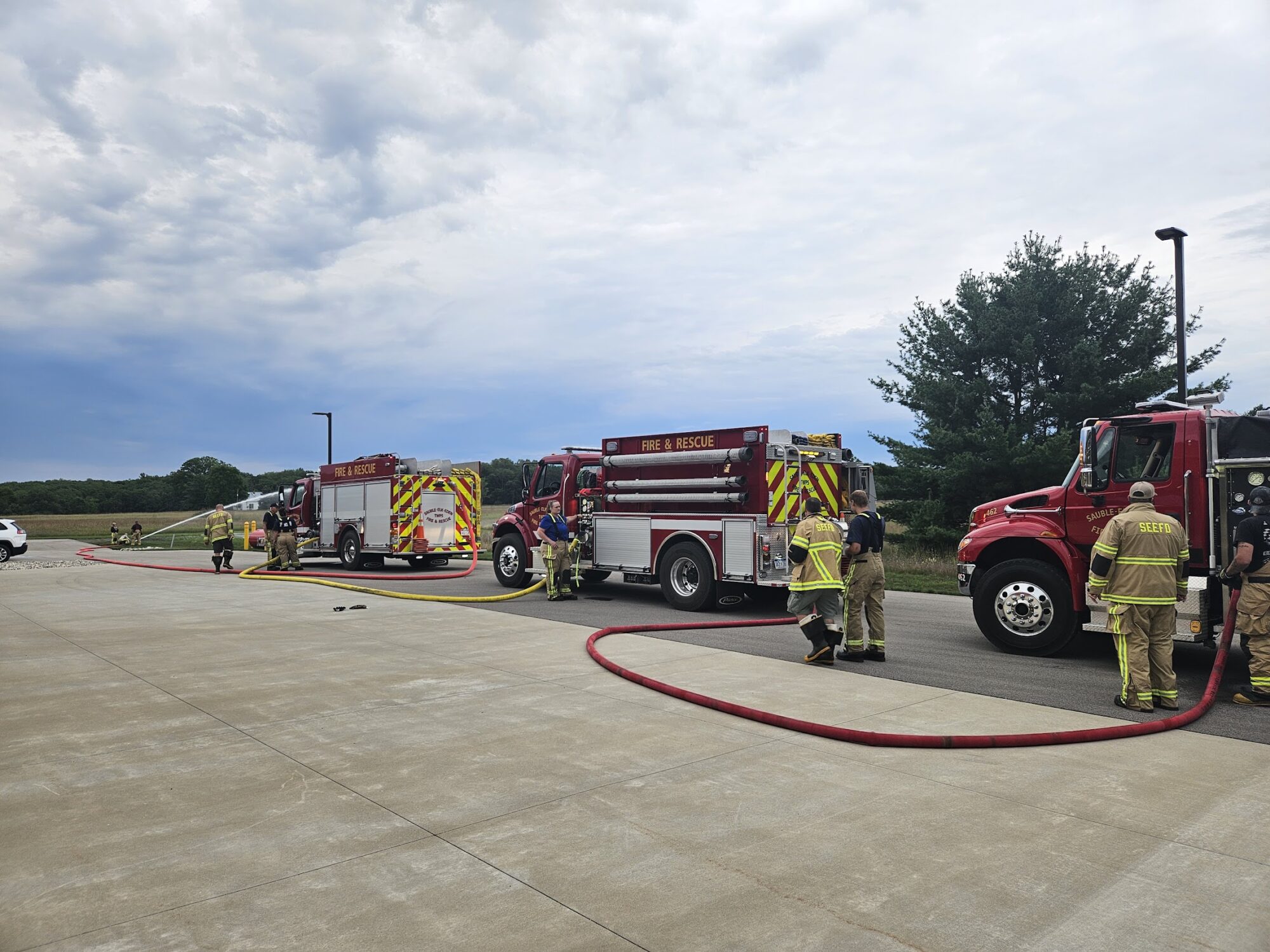 Firefighters with trucks and hoses, outdoor training scene.