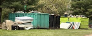 Discarded furniture and mattresses by dumpsters in park.